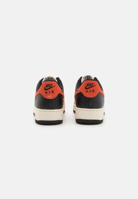 Zapatillas Nike Air en negro y naranja con parte superior de cuero, cuello acolchado y suela de goma con agarre texturizado y detalle del logotipo en el talón.