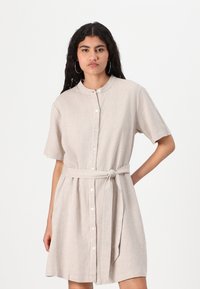 Beige linen shirt dress with short sleeves, a mandarin collar, front button closure, and a tied waist belt, featuring a relaxed fit and above-knee length.