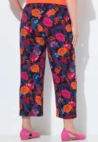 Pantalons met bloemenprint in paars met heldere oranje, roze en blauwe bloemen. Heeft een relaxte pasvorm en een cropped lengte, gecombineerd met roze schoenen.