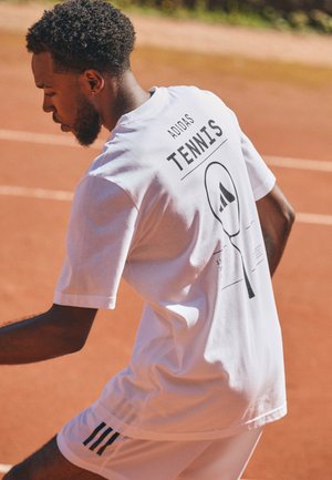 White short-sleeve t-shirt featuring black graphics, including "TENNIS" and a racket design, paired with white shorts bearing black stripes.