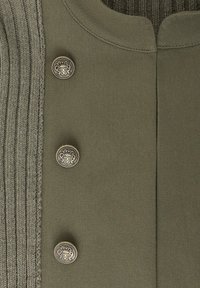 Gros plan sur un tissu vert olive avec trois boutons métalliques décoratifs ornés d’un blason et une bordure côtelée tricotée le long du bord.