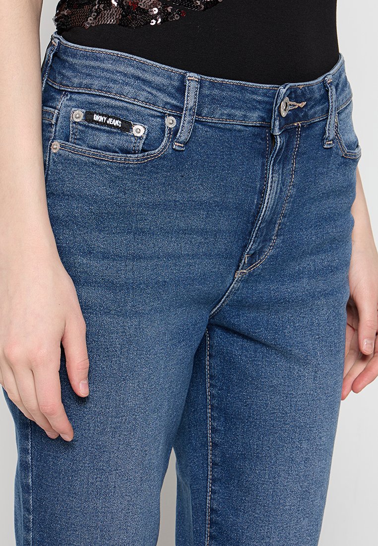Jeans in denim blu con una vestibilità slim, dotati di tasche frontali, etichetta con marchio e cuciture visibili. Il tessuto ha una texture liscia.