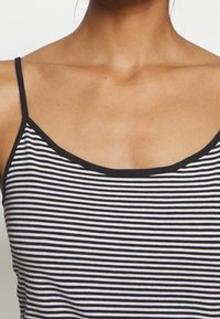 Mujer con una blusa sin mangas de rayas blancas y negras, mostrada desde el cuello hasta el torso.