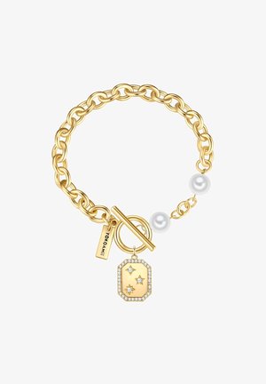 Brăţară din metal de culoare aurie cu închidere tip toggle, având un charm decorat cu pietre transparente şi un eticheta marcată "YOKO AMI," plus două perle albe.