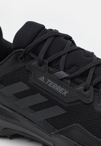 Czarne buty sportowe z siateczkowym wierzchem, wzmocnionym palcem, sznurowaniem i gumową podeszwą. Posiadają wyraźny design z trzema paskami w macie czarnym.