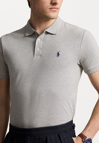 Szara koszulka polo wykonana z teksturowanej tkaniny, z trzema guzikami i małym niebieskim haftowanym logo po lewej stronie klatki piersiowej.
