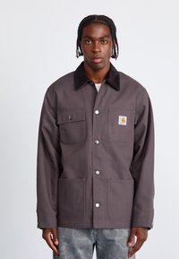 Grå lærredjakke med sort fløjlskrave, to frontlommer og knaplukning. Har et lille Carhartt-logo på brystlommen.