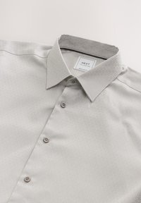 Light gray button-up shirt with a subtle texture, featuring a classic collar, four buttons, and a label reading "NEXT Tailoring, Regular Fit."