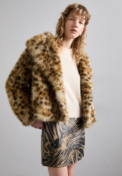 Faux fur takki ruskealla ja khakivärisellä leopardikuviolla, jossa on rento istuvuus. Vaatteena vaaleancremepaitapaidan päällä ja kuviollisen, vartaloa myötäilevän hameen kanssa.