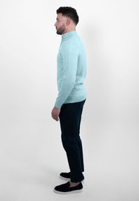 Lichtblauwe zip-up sweater, geribde zoom, gecombineerd met donkere broek en zwarte instappers. Textuur lijkt glad en aansluitend.