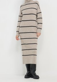 Abito a collo alto beige a righe con righe orizzontali nere, polsini a coste e una vestibilità lunga e slim, abbinato a stivali neri al ginocchio.