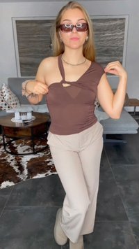 Brown, one-shoulder top with a cutout detail, paired with cream trousers. The top has a smooth texture; the trousers are loose-fitting.