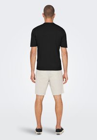 Black short-sleeve shirt with a crew neckline, paired with light, striped shorts and black shoes. Background is plain white.