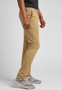 Khaki chinot, jossa on kapea malli, litteä etuosa ja sileä puuvillakangas. Yhdistetty harmaisiin urheilukenkiin, joissa on valkoisia yksityiskohtia ja nauhoja.