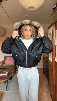 Jachetă neagră scurtă, cu glugă căptușită cu blană, prevăzută cu două buzunare frontale, închidere cu fermoar și manșete elastice. Purta peste un tricou alb.