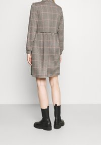 Robe en damier noir et blanc avec manches longues, taille cintrée et coupe au genou, associée à des bottines noires.