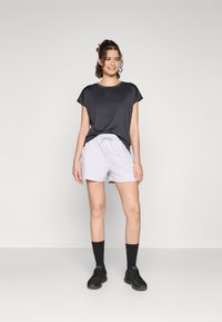 Camiseta negra de manga corta, pantalones cortos de cintura con cordón en gris claro, calcetines negros y zapatillas deportivas negras. Tejido suave, corte relajado.