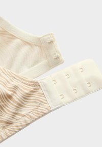Sujetador beige con un patrón ondulado texturizado, cuenta con cierres ajustables de gancho y ojal y una banda suave y lisa.