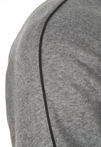 Gros plan sur un sweat-shirt gris, présentant une texture lisse avec une couture noire contrastante le long de l'épaule. Design simple et moderne.