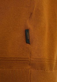 Pullover arancione a maglia con finitura testurizzata, orlo a coste e una piccola etichetta nera con la scritta "CHASIN'" stampata in arancione.