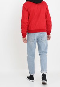 Rode suède bomberjack met geribbelde manchetten en zoom, gecombineerd met lichtblauwe denim jeans en zwarte high-top sneakers.