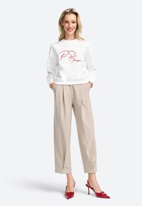 Felpa bianca con scritta rossa "PS I love you," abbinata a pantaloni beige chiaro plissettati e décolleté in vernice rossa.
