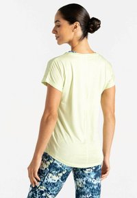 Camiseta deportiva de color amarillo claro con mangas cortas, textura suave y cuello redondeado, combinada con leggings azules estampados que presentan un diseño multicolor.