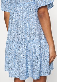 Ljusblå klänning med korta ärmar, med ett blommönster i vitt och svart, lager-på-lager volang nederkant, och mjukt, texturerat tyg.