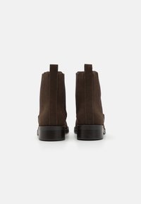 Brune semskede ankelstøvler med elastiske sidedele, trækflapper og chunky træsko, der har en glat overflade og et enkelt design.