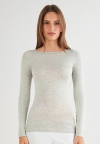 Lange mouwen top in lichtgrijs, gemaakt van zacht breimateriaal. Heeft een bootnek en een aangesloten silhouet. Minimalistisch ontwerp zonder patronen.