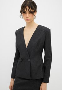 Donkergrijze getailleerde blazer met een diepe V-hals, lange mouwen, dubbele knoopsluiting en een gestructureerde stof. Eenvoudig, gestructureerd ontwerp.