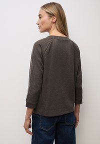 Brauner, langärmeliger Sweatshirt mit lässigem Schnitt. Verfügt über Raglanärmel und weiße Streifen entlang der Ärmel. Kombiniert mit blauen Jeans.