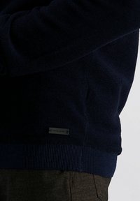 Navyblauer Strickpullover mit strukturiertem Muster, ausgestattet mit gerippten Bündchen und Saum. Enthält ein Metallschild mit dem Branding "pierre cardin".