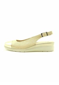 Sandalia cuña tipo slingback en crema. Presenta un upper de malla texturizada, punta metálica y un cierre de hebilla ajustable. Tacón cuña para mayor soporte.