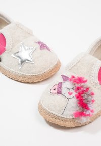 Chaussons en feutre gris clair avec des accents roses. Présente des applications en étoile argentées et roses ainsi qu'un design de licorne avec des détails texturés et des fibres pastel.