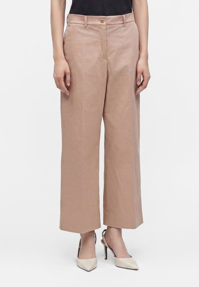 Pantalon beige à coupe large et courte avec bouton devant et passants de ceinture, porté avec des chaussures à talons hauts pointues beiges et un top noir.