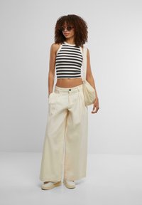 Black and white striped crop top, cream wide-leg trousers, and white sneakers. Adjustable strap tote bag with a quilted texture.