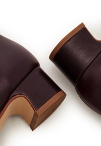 Bordowe skórzane botki za kostkę z okrągłym noskiem i masywnym brązowym obcasem. Gładka tekstura, minimalistyczny design, brak widocznych elementów metalowych lub wzorów.