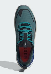 Green hiking shoe features a mesh upper with dark accents, turquoise laces, and a black interior. Includes a pull tab and cushioned sole.