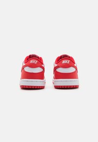 Červené a biele Nike tenisky s polstrovaným golierom, gumovou podrážkou a minimálnym brandingom na päte. Hladká textúra, atletický dizajn.