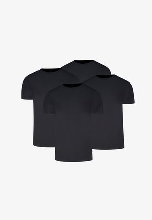 Mann trägt ein schlichtes schwarzes kurzärmeliges T-Shirt und hellgraue, eng anliegende Boxershorts, steht vor einem einfarbigen hellen Hintergrund.