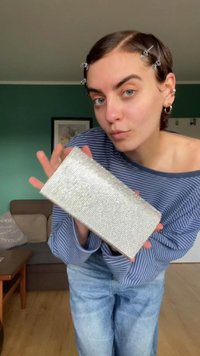 Bolso de mano rectangular plateado metálico adornado con pequeños strass. Textura suave, diseño minimalista y forma compacta.