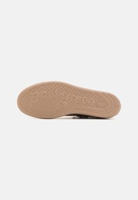 Semelle de chaussure brune en caoutchouc beige clair texturé. Présente un motif circulaire et un nom de marque en relief, offrant une bonne adhérence.
