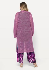 Cardigan largo y abierto hecho de tejido de malla púrpura con un corte holgado. Combinado con pantalones de pierna ancha de colores púrpura, negro y blanco y tacones plateados.