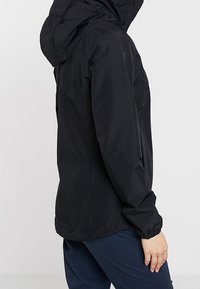 Svart vattentät jacka med huva, med elastiska manschetter, avslappnad passform och slät textur; designad för funktionalitet och skydd.