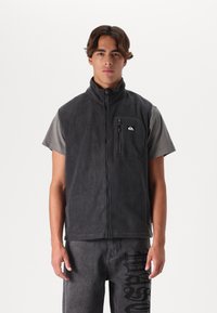 Gray fleece vest with high collar, full zipper, front pocket, paired with a short-sleeve gray shirt and dark gray pants featuring black print.