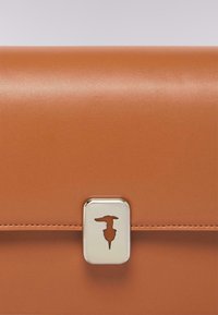 Nahaufnahme des Klappens eines braunen Lederbeutels mit einem silbernen rechteckigen Verschluss, der ein durchbrochenes Schlüssellochdesign aufweist.