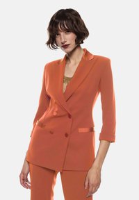 Blazer arancione doppiopetto con colletto a pisano, maniche a tre quarti e due tasche anteriori, realizzato in tessuto liscio.