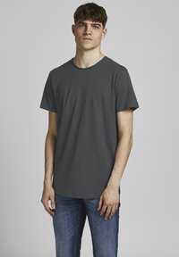 Camiseta gris de manga corta con cuello redondo, hecha de una tela suave. Se lleva con jeans azules, que tienen un corte casual y detalles de costura mínimos.