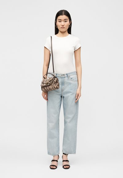 Γυναίκα φοράει λευκό εφαρμοστό t-shirt, ανοιχτό μπλε τζιν με ψηλή μέση, μαύρα σανδάλια με ανοιχτά δάχτυλα, κρίκους σκουλαρίκια και τσάντα χιαστί με σχέδιο ζέβρας.